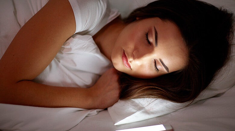 mujer acostada en cama con el celular