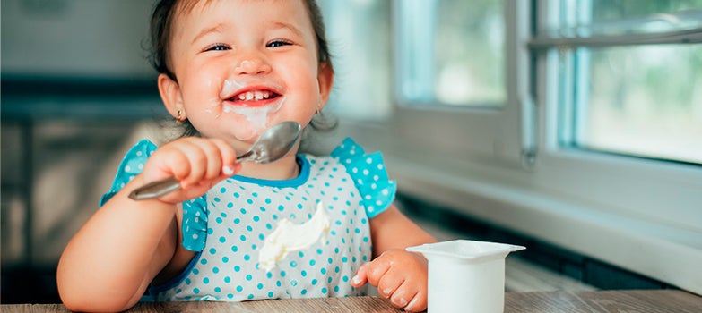 bebé sonriente comiendo sola con su ropa manchada