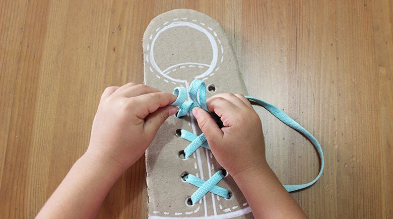 Niño aprendiendo a amarrarse los zapatos con la ayuda de su padre