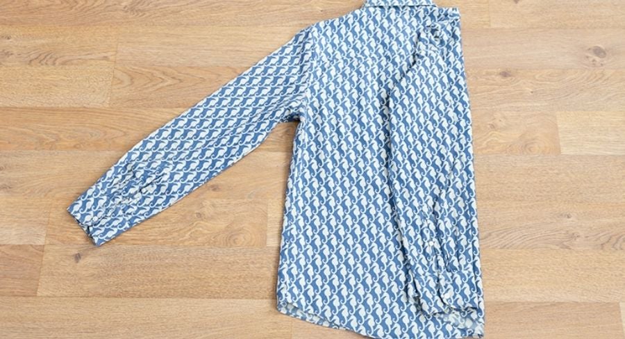 Proceso para doblar una camisa: Acomoda la manga a lo largo del doblez