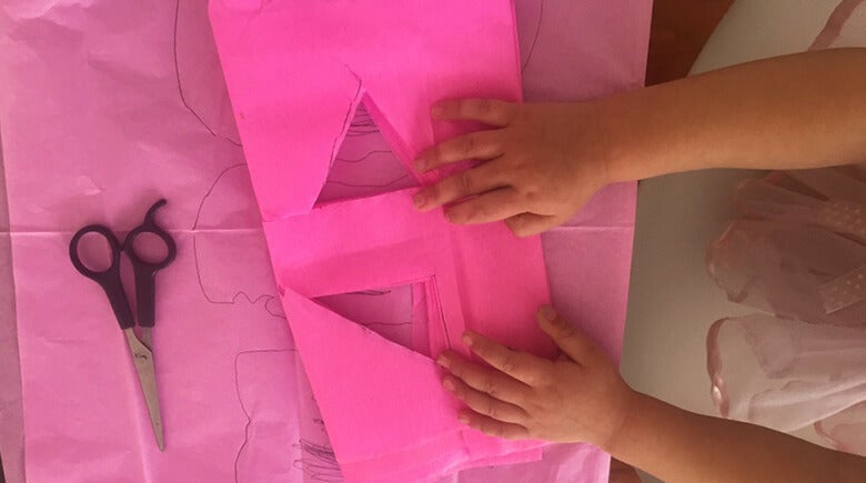 Niña cortando un papel rosa