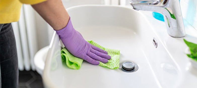 Persona limpiando el lavamanos del baño con vinagre blanco para mantenerlo impecable y libre de manchas
