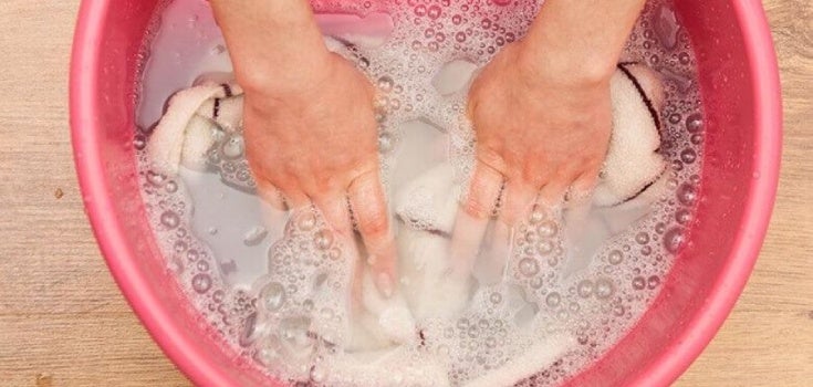 Manos restregando ropa con jabón y agua dentro de un tazón