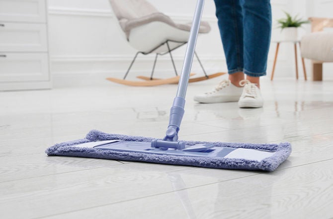 Persona usando mopa plana para limpiar y abrillantar pisos de cerámica blanca en la sala.